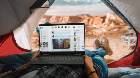 Photo for POV of a Tourist Using a Laptop Computer for Checking Social Network Feed and Latest Photos. Traveller Resting in a Tent on Top of Rocky Mountain. Adventurous Hiker Living in Nature in Great Outdoors. - Royalty Free Image