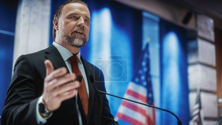 Photo for Portrait of Organization Representative Speaking at a Press Conference in Government Building. Press Officer Delivering a Speech at a Summit. Minister at Congress. Backdrop with American Flags. - Royalty Free Image