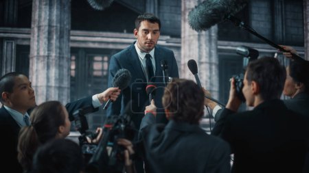 Photo for Young Organization Representative Answering Press Questions and Giving Interview Outside a Parliament, Court or Other Government Building. Press Officer or Businessman Crowded by News Journalists. - Royalty Free Image