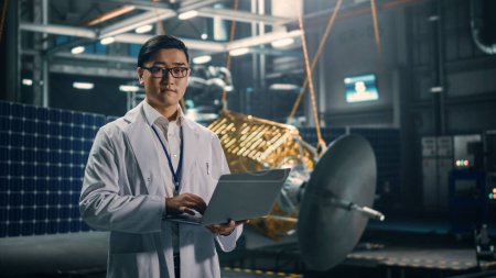 Téléchargez les photos : Portrait d'un ingénieur asiatique sérieux travaillant sur la construction de satellites artificiels. Agence aérospatiale : Scientifique chinois utilisant un ordinateur portable pour développer des engins spatiaux pour l'exploration spatiale. - en image libre de droit