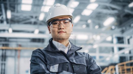 Téléchargez les photos : Portrait d'un ingénieur asiatique professionnel de l'industrie lourde portant un uniforme de sécurité, des lunettes et un casque rigide, regardant dans la caméra. Spécialiste industriel chinois confiant debout dans une usine. - en image libre de droit