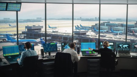 Téléchargez les photos : Équipe de contrôle de la circulation aérienne diversifiée travaillant dans une tour d'aéroport moderne. La salle de bureau est pleine d'écrans d'ordinateur de bureau avec des écrans de navigation, des données de départ et d'arrivée d'avion pour les contrôleurs. - en image libre de droit