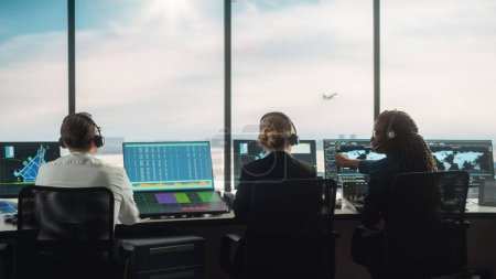 Foto de Equipo de Control de Tráfico Aéreo Diverso Trabajando en una Torre Moderna del Aeropuerto. La sala de oficina está llena de pantallas de computadora de escritorio con pantallas de navegación, salidas de aviones y datos de llegada para controladores. - Imagen libre de derechos