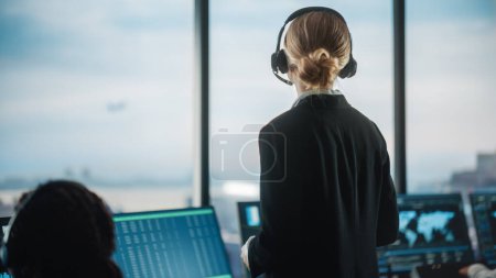 Fluglotsin mit Headset-Talk bei einem Anruf im Flughafen-Tower. Der Büroraum ist voll mit Desktop-Computer-Displays mit Navigationsbildschirmen, Flugzeug-Radardaten für das Team.