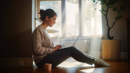 Photo for Young Woman Using Laptop at Home for Remote Work. Beautiful Girl Sitting on the Floor Uses Internet, Drinks Morning Cup of Coffee. Sunny Morning Good for Productive Distant Work - Royalty Free Image