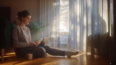 Photo for Beautiful Happy Woman Using Laptop at Home for Remote Work. Young Adult Smiling Woman Sitting on the Floor Uses Internet, Writes Report, Finishes Project. Good Sunny Day for Productive Distant Work - Royalty Free Image