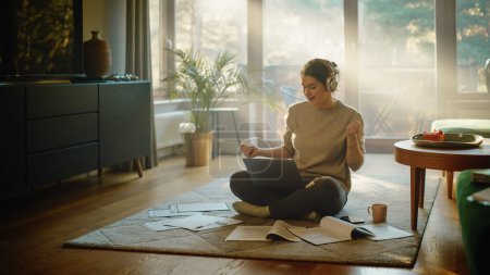 Photo for Young Woman Using Laptop at Home, Does Remote Work, Listens Music through Headphones. Beautiful Smiling Girl Sitting on the Floor Does Research on Papers, Documents, Brainstorms Creative Project - Royalty Free Image