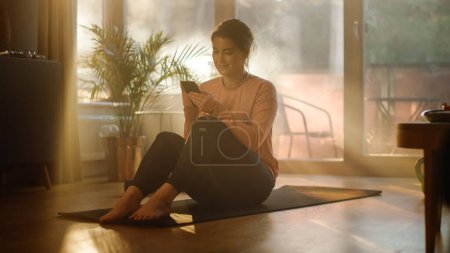 Photo for Beautiful Girl Using Smartphone after Fitness Workout at Home. Authentic Plus Size Woman Using Fitness Tracker, Yoga Exercises Application, Browsing Online Health Articles, Posting on Internet - Royalty Free Image