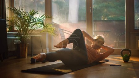 Photo for Beautiful Girl Doing Fitness Exercises at Home. Authentic Determined Woman Doing Workout, Side Crunches, Yoga Exercises. Healthy Fit Confident Female. Sunny Living Room - Royalty Free Image