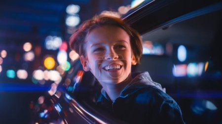 Aufgeregter Junge sitzt auf dem Rücksitz eines Autos und pendelt nachts nach Hause. Mit Erstaunen aus dem Fenster schauen, wie schön die Stadtstraße mit den funktionierenden Leuchtreklamen ist.