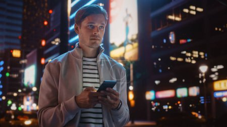 Photo for Handsome Blonde Man Standing on a Street of a Night City. Thoughtful Attractive Young Man Traveling, Looking Around Urban Center Contemplating Business Ideas, Future Career. Air of New Possibilities - Royalty Free Image