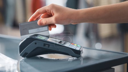 Photo for Clothing Store: Customer at Counter Buys Clothes Paying with Credit Card Through Wireless NFC Bank Terminal. Trendy Fashion Shop with Stylish Designer Brands. Close-up Focus on Hand. - Royalty Free Image