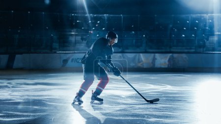 Foto de Ice Hockey Rink Arena: Entrenamiento de Jugadores Profesionales Solos. Skates, Practices Shooting, Hitting, Stricking the Puck with Hockey Sticks (en inglés). Deportista decidido con deseo de ganar, ser campeón. - Imagen libre de derechos