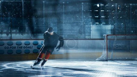 Foto de Ice Hockey Rink Arena: Entrenamiento de Jugadores Profesionales Solos. Skates, Practices Shooting, Hitting, Stricking the Puck with Hockey Sticks (en inglés). Deportista decidido con deseo de ganar, ser campeón. - Imagen libre de derechos
