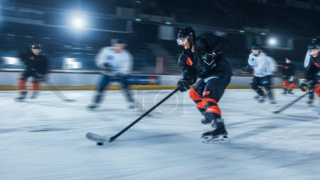 Foto de Ice Hockey Rink Arena: Jugador profesional delantero rompe la defensa, golpeando Puck con palo para marcar un gol. Disparo de movimiento borroso. - Imagen libre de derechos