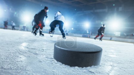 Foto de Primer plano Shot with Focus on a 3D Hockey Puck on Ice Hockey Rink Arena. En el fondo borrosa jugadores profesionales de diferentes equipos tratando de conseguir el Puck. Disparo de ángulo holandés. - Imagen libre de derechos