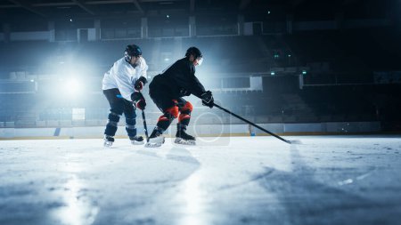 Foto de Arena de pista de hockey sobre hielo: Dos jugadores jóvenes entrenando, aprendiendo palillo y manejo de pato. Los atletas aprenden a driblar, atacar, defender, proteger, poseer, conducir el pato. - Imagen libre de derechos