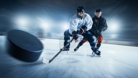 Blurred Motion Shot mit 3D Flying Puck. Zwei Eishockeyprofis aus verschiedenen Teams kämpfen in der Arena mit Stöcken um den Puck. Sportler spielen ein intensives Spiel im Energiewettbewerb