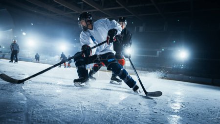 Foto de Ice Hockey Rink Arena: Dos jugadores profesionales de diferentes equipos que luchan por el Puck con palo durante el campeonato. Los atletas juegan intenso juego amplio de la competencia de energía. Disparo de ángulo holandés bajo. - Imagen libre de derechos