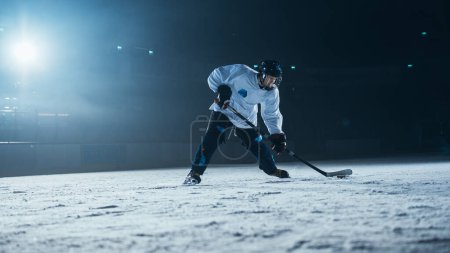 Téléchargez les photos : Patinoire de hockey sur glace : entraînement professionnel seul. Patins, dribble avec bâton, frapper la rondelle. Athlète déterminé avec le désir de gagner, être champion. - en image libre de droit