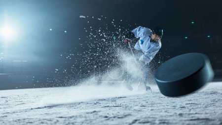 Photo for Ice Hockey Rink Arena: Professional Player Shooting the Puck with Hockey Stick. Focus on 3D Flying Puck with Blur Motion Effect. Dramatic Wide Shot, Cinematic Lighting. - Royalty Free Image