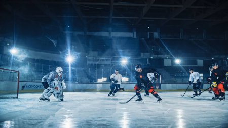 Eishockey-Arena: Profi-Stürmer durchbricht Abwehr und bereitet Puck mit Stock zum Tor vor Zwei konkurrenzfähige Teams spielen ein intensives Spiel.