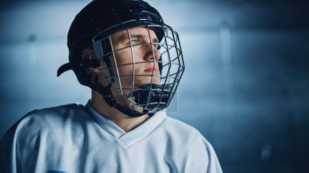 Foto de Arena de pista de hockey sobre hielo: Retrato de jugador profesional confiable, usando máscara facial de jaula de alambre, mirando lejos. Atleta enfocado, decidido a ganar y ser campeón. Tiro de retrato - Imagen libre de derechos