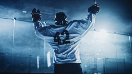 Eishockey-Spiel: Profispieler feiert Sieg auf der Eisbahn, hebt die Arme Junger Sportler wurde durch Anstrengung und Zielstrebigkeit zum Champion.