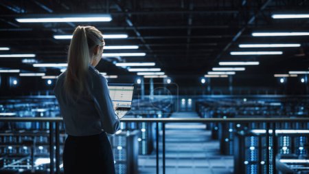 Photo for Data Center Female IT Specialist Uses Laptop Computer. Cloud Computing Server Farm with IT Engineer Monitoring Statistic, Maintenance Control. Information Technology of Fintech, e-Business. - Royalty Free Image