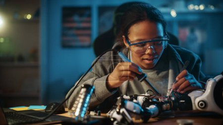 Foto de Young Teenage Multiethnic Schoolgirl está estudiando electrónica y soldadura de cables y placas de circuitos en su proyecto de robótica de ciencia Hobby. Chica está trabajando en un robot en su habitación. Concepto de educación. - Imagen libre de derechos