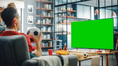 Photo for At Home Joyful Soccer Fans Sit on a Couch Watch Green Screen Chroma Key Screen. Friends Cheer for Favourtite Football Sports Team to Win Championship. Over the Shoulder - Royalty Free Image