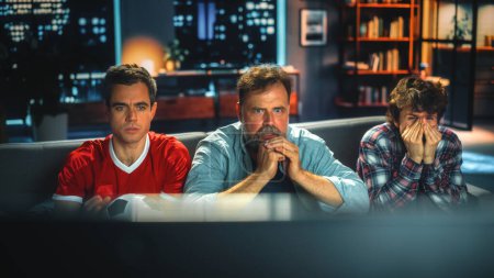 Photo for Night At Home: Three Joyful Soccer Fans Sitting on a Couch Watch Game on TV, Worry and Tense Moment. Sports Team Wins Championship. Group of Friends Cheer for Favourite Football Club Play - Royalty Free Image