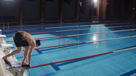 Muskulöse ältere männliche Schwimmer stehen auf einem Startblock und bereiten sich auf den Sprung ins Schwimmbad vor. Gesundes professionelles Athletentraining für die WM. Schuss mit Sonnenbrille