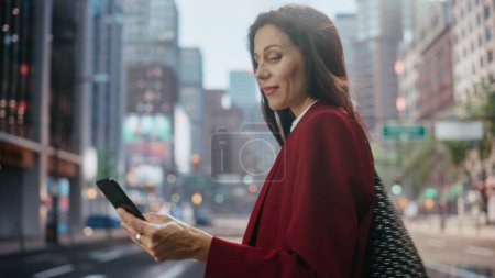 Téléchargez les photos : Portrait d'une femme d'affaires adulte attrayante utilisant un ordinateur tablette dans la rue dans une grande ville. Gestionnaire confiant Connexion avec les gens en ligne, Messagerie, Naviguer sur Internet sur son chemin vers le bureau. - en image libre de droit