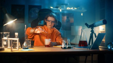 Foto de Smart Young Boy en gafas de seguridad mezcla productos químicos en vasos de precipitados en casa. Adolescente llevando a cabo experimentos de ciencia educativa Hobby, haciendo interesantes tareas de biología en su habitación. - Imagen libre de derechos