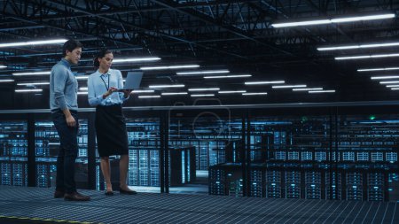 Photo for Data Center Female System Administrator and Male IT Specialist Talk, Use Laptop Computer. Information Technology Engineers work on Cyber Security Network Protection in Cloud Computing Server Farm. - Royalty Free Image