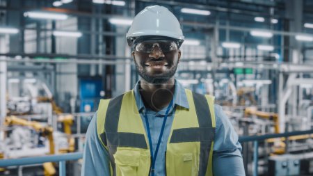 Photo for Portrait of an Automotive Industry Engineer in Safety Uniform Smiling at Car Factory Facility. Happy Assembly Plant African American Male Specialist Working on Manufacturing Modern Electric Vehicles. - Royalty Free Image