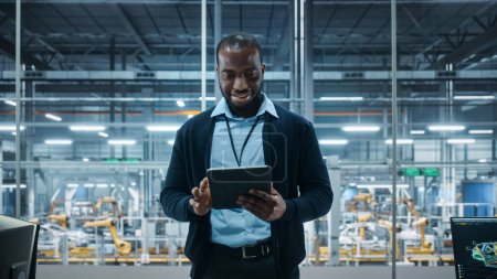 Photo for Car Factory Office: Portrait of Successful Black Male Chief Engineer Using Tablet Computer in Automated Robot Arm Assembly Line Manufacturing High-Tech Electric Vehicles. Medium Shot - Royalty Free Image