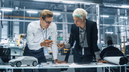 Zwei junge Kfz-Ingenieure arbeiten im Büro in der Autofabrik. Industriedesigner und Kollege diskutieren unterschiedliche Anwendungen eines Metall-Ritzelgetriebes in persönlichen Mobilitätsfahrzeugen.