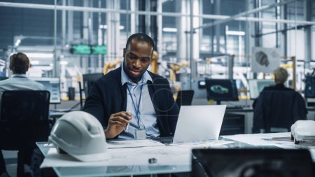 Jeune ingénieur afro-américain travaillant sur ordinateur portable dans un bureau à l'usine d'assemblage de voitures. Spécialiste industriel travaillant sur les pièces de véhicules dans une installation de développement technologique.