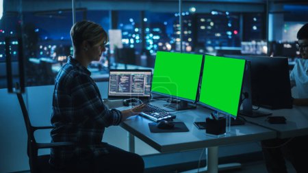 Photo for Diverse Teamwork in Office at Night: Person with Disability Using Prosthetic Arm to Work on Green Screen Chroma Key Computer. Team of Software Engineers work Late to create Innovative App - Royalty Free Image