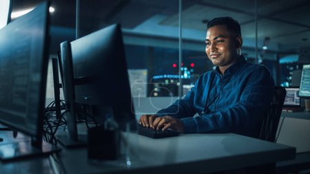 Photo for Night Office: Portrait of Handsome Indian Man in Working on Desktop Computer. Digital Entrepreneur Typing, Creating Software, e-Commerce App Design, Programming. Thoughtful Happy Man Finding Solution - Royalty Free Image