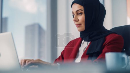 Photo for Close-up Portrait of Gorgeous Muslim Businesswoman Wearing Burka Sitting at Her Desk Working on Laptop Computer in Office. Successful Corporate CEO Plan Investment Strategy for e-Commerce Startup - Royalty Free Image