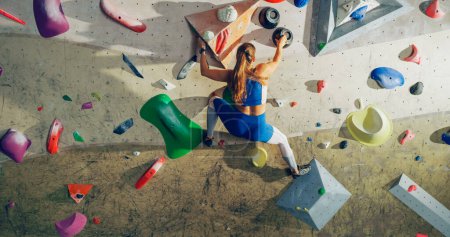 Athletic Female Rock Climber Practicing Solo Climbing on Bouldering Wall in a Gym. Female Exercising at Indoor Fitness Facility, Doing Extreme Sport for Her Healthy Lifestyle Training. Shot from Back.