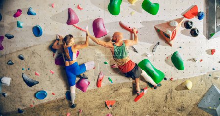 Zwei erfahrene Kletterer üben das Klettern an der Boulderwand in einer Sporthalle. Friends Turnen im Indoor-Fitnessstudio, Extremsport für ein gesundes Training. Sich gegenseitig hoch fünf geben.