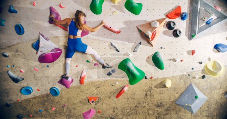 Sportliche Bergsteigerin beim Solo-Klettern an der Boulderwand in einer Turnhalle. Frauentraining im Indoor-Fitnessstudio, Extremsport für ihr gesundes Lifestyle-Training. Schuss von hinten.