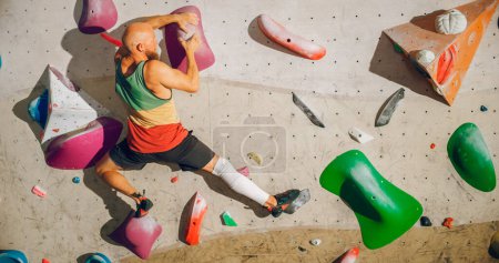 Starker erfahrener Bergsteiger übt sich im Solo-Klettern an der Boulderwand in einer Turnhalle. Der Mann trainiert in einem Indoor-Fitnessstudio und macht Extremsport für sein gesundes Lifestyle-Training. Schuss von hinten.