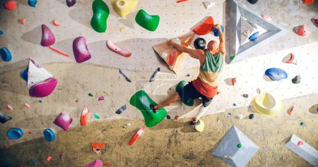 Photo for Strong Experienced Rock Climber Practicing Solo Climbing on Bouldering Wall in a Gym. Man Exercising at Indoor Fitness Facility, Doing Extreme Sport for His Healthy Lifestyle Training. Shot from Back. - Royalty Free Image