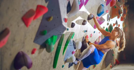 Sportliche Bergsteigerin übt sich im Solo-Klettern an der Boulderwand in der Sporthalle. Frauentraining im Indoor-Fitnessstudio, Extremsport für ihr gesundes Lifestyle-Training. Porträt aus nächster Nähe
