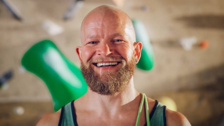 Photo for Strong Masculine Male Athlete Smiling and Posing at Rock Climbing Gym with Bouldering Wall Background. Handsome Happy Bald Man with Ginger Beard Portrait, Wearing Colorful Undershirt. - Royalty Free Image